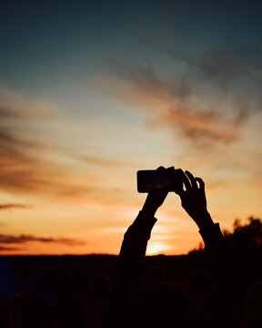 Silhouette of the hands of a person with a mobile phone taking a picture at sunset. Natural sunset background with orange tones.