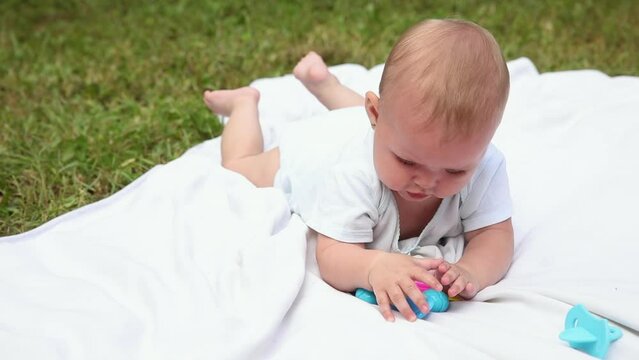 Little newborn girl lying on tummy chewing rattle on blanket, summer day outdoor. Infant having fun outdoors. Infant baby child resting playing learning to crawl. Motherhood teething, babyhood concept