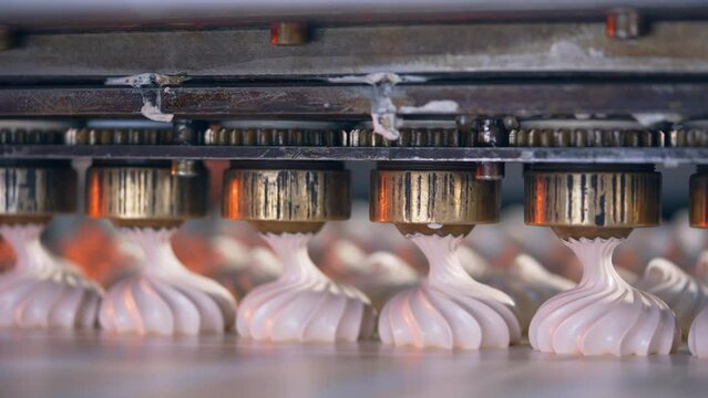 Rotating metal nozzles lay creamy substance on the conveyor belt to create beautifully-shaped marshmallows. Close up. Food factory concept.