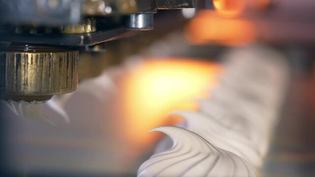 Whipped white vanilla cream comes out off a metal nozzle. Freshly squeezed marshmallows on the conveyor belt. Close up.