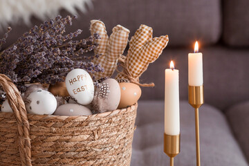 Provence. A wicker basket with Easter eggs, lavender and burning candles in the interior of the living room on a wooden table. The concept of home comfort in the bright holiday of Easter 2022.