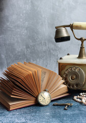 Vintage phone, open book, old keys, and retro pocket watch on a desk. Nostalgic composition image. 