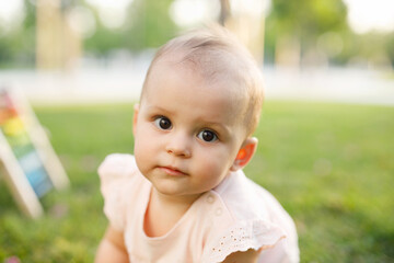 Cute little girl outside in nature on a summer day. Sweet toddler girl on fresh green grass plaing in summer park. Portrait of child.