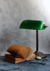 Still life with vintage green lamp, opened book and glasses. Simple composition photo. Retro objects close up. Education concept.