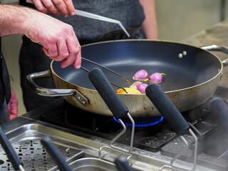 chef cooking and grilling onions and a golden  potato on a pan in a professional restaurant...