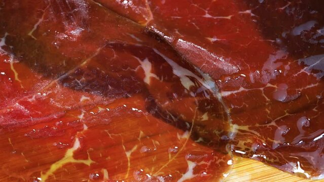 pouring olive oil on smoked red meat, close up view. Macro shot of spanish traditional cecina with golden olive oil on top.