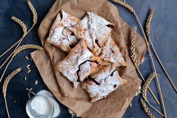 Appetizing pastries in the form of envelopes with powdered sugar and spikelets of wheat on a dark...