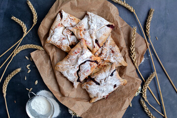 Appetizing pastries in the form of envelopes with powdered sugar and spikelets of wheat on a dark gray background. View from above