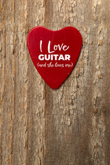 Red heart shaped guitar pick on wooden table with text I love guitar and she loves me