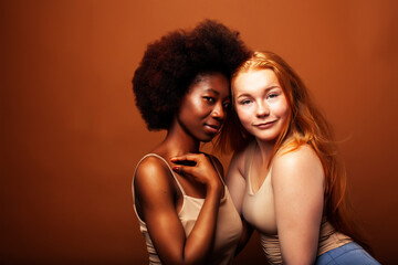 young pretty african and caucasian women posing cheerful together on brown background, lifestyle diverse nationality people concept