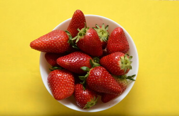 Big red strawberries on white plate on yellow background close up. Fresh ripe strawberries The concept of the benefits of ripe summer berries. 