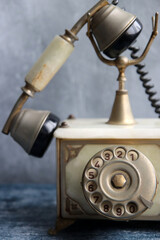 Old fashioned rotary phone on a table. Vintage telephone close up photo. Grey textured background with copy space.
