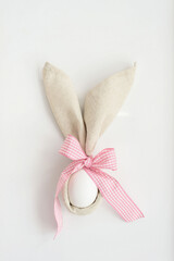 Fototapeta na wymiar Easter table setting, easter egg in linen napkins like bunny ears with pink bow on white background. Idea Easter decor.