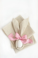 Easter table setting, easter egg in linen napkins like bunny ears with pink bow on white background. Idea Easter decor.