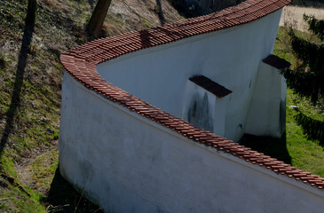 defensive wall of the castle with loopholes. zigzagging white wall with roof tiles roofing. under...