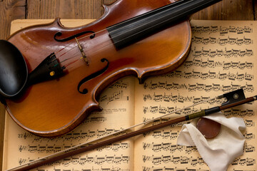 Stare skrzypce ze smyczkiem na tle nut i drewnianych desek.