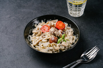 pasta with meatballs from plant-based meat, mushrooms, creamy sauce, tomatoes on a dark concrete background. copy space