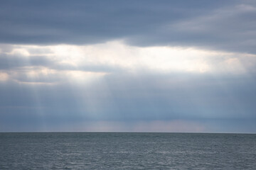 Calm seascape with stormy sky where sun-rays get through the clouds.
