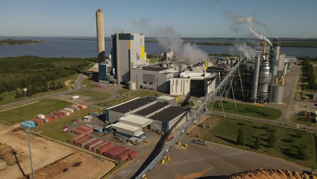 Smoking chimneys in paper mill factory at Fray Bentos along Uruguay river. Aerial circling