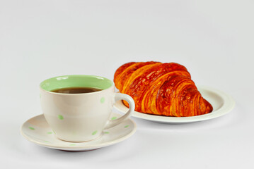Yellow croissant in a plate and coffee isolated on a white background. Classic breakfast close up.