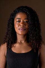 Mid waist portrait of african american woman with dark hair and serious look. Vertical front view of african woman with sad expression in brown background. People diversity concept.