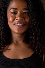 Cropped portrait of african american woman with dark hair and white cheerful smile. Vertical closed up view of african woman with happy expression in brown background. People and color concept.