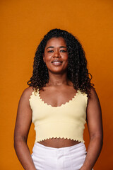 Mid waist portrait of african american woman with dark hair and orange clothes. Vertical front view of african woman with happy expression in orange background. People and color concept.