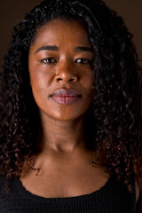 Cropped portrait of african american woman with dark hair and calm expression. Vertical closed up view of african woman with sad expression in brown background. People and color concept.