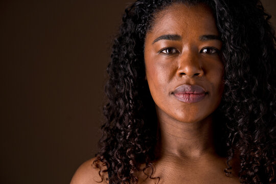 Mid waist portrait of african american woman with dark hair and serious look. Horizontal front view of african woman with sad expression in brown background. People diversity concept.