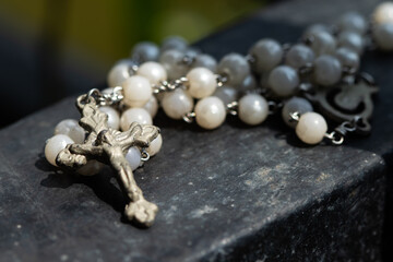 Rosary with a cross made of white beads on an iron fence.