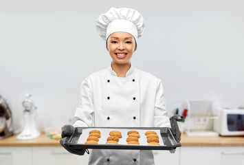 cooking, culinary and bakery concept - happy smiling female chef or baker in toque holding baking tray with oatmeal cookies over kitchen background