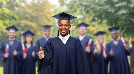 education, graduation and people concept - happy graduate student woman in mortarboard and bachelor gown giving her hand for handshake over group of bachelors at park on background