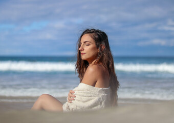 Fototapeta na wymiar Beautiful brunette woman with eyes closedsunbathing on the beach and having cold