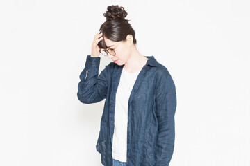 白い背景の前に立っている発熱で額に手を当てる眼鏡をかけている女性