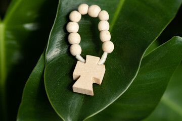 Cross and rosary in ring shape on green plant leaf.