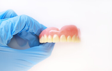 An acrylic denture in a gloved hand. Doctor's hand holds a denture. Set of false teeth.