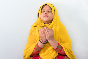 A religious Asian Muslim child girl in the Muslim hijab dress is praying to Allah or God during the Ramadan period