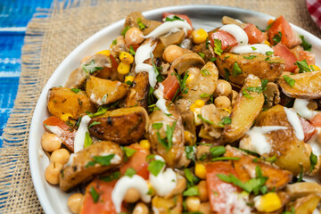 close-up of A delicious potato, chickpea, tomato and mushroom salad with parsley and aioli in a bowl on a wooden table. Healthy, homemade, vegan food.