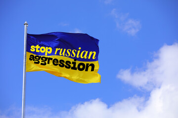Waving Ukrainian flag with text STOP RUSSIAN AGGRESSION against blue sky