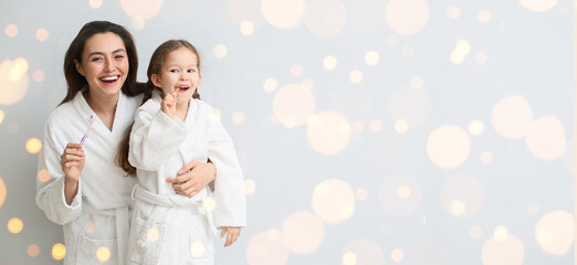 Little girl and her mother brushing teeth on light background with space for text