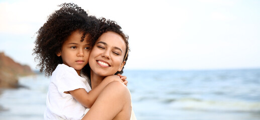 African-American girl and her mother hugging on sea beach