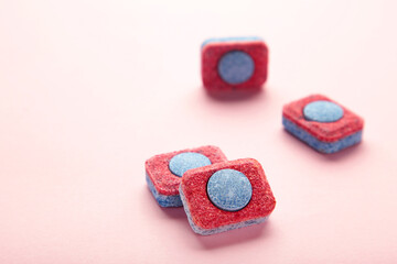 Red and blue tablets for dishwashing machine. Detergents for home hygiene. Dishwasher capsules on pink background.