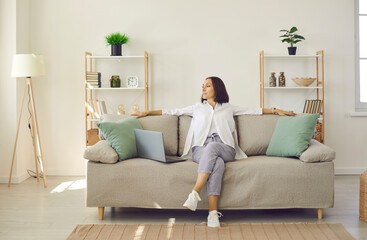 Home office. Happy beautiful senior woman sitting on sofa at home resting after working on laptop. Entrepreneur working at home looking away thinking about something nice. Successful business concept.