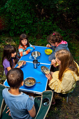 Kids eating on a blue camping table. Outdoor recreation. Children's picnic on a background of greenery.