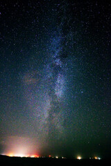 Vertical shot of the night sky where Milky Way can be seen with city lights seen from afar
