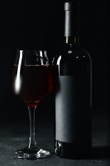 Glass and bottle of tasty red wine on dark background