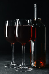 Glasses and bottle of tasty red wine on dark background