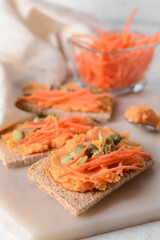 Board with crispbreads and tasty carrot hummus on table