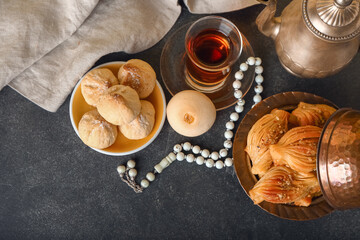 Tasty Eastern sweets and tea with tasbih on dark background
