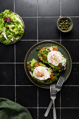 toast with poached egg, lettuce, tomato and capers on a dark background, top view